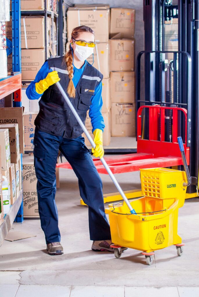 pexels-photo-209271-209271 Female janitor in safety gear cleaning a warehouse floor with a mop and bucket.