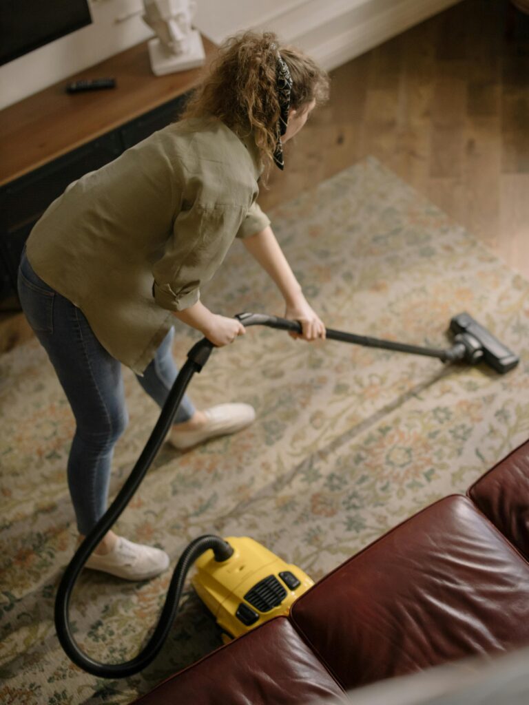pexels-photo-4107286-4107286 High-angle view of a woman vacuuming a patterned carpet in a stylish living room.
